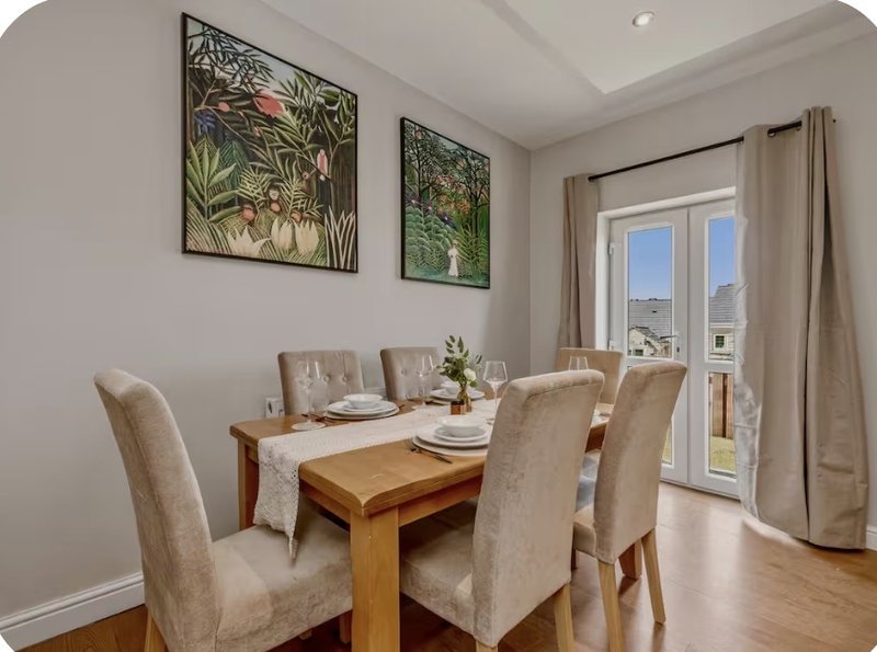 Dining room with wooden table, four beige chairs, botanical wall art, and glass doors to balcony