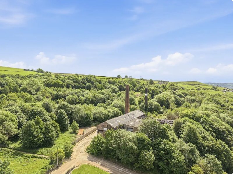 Aerial view of rural property with barn, surrounded by green fields and woodland