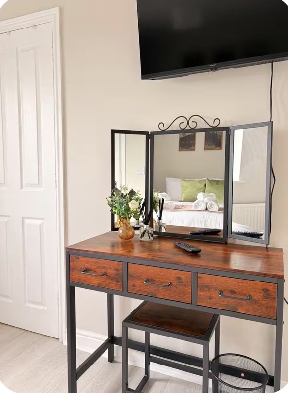 Bedroom dressing table with mirror, wooden drawers, potted plant and mounted television above