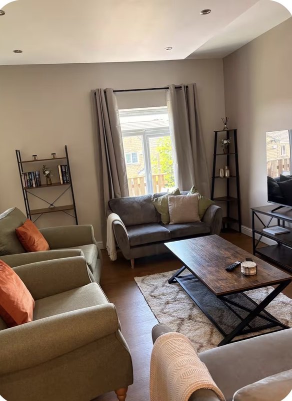 Bright living room with beige armchairs, dark sofa, wooden coffee table, and window with garden view