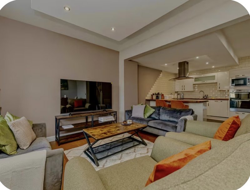 Open-plan living room with beige sofas, wooden coffee table, TV, and kitchen visible in background