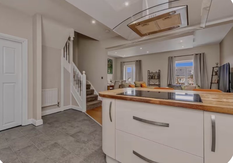 Modern open-plan kitchen and living area with white cabinetry, wooden countertop, staircase, and city views