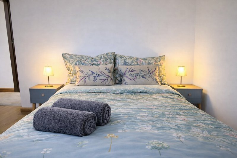 Modern bedroom with double bed, rolled towels, decorative pillows and bedside lamps