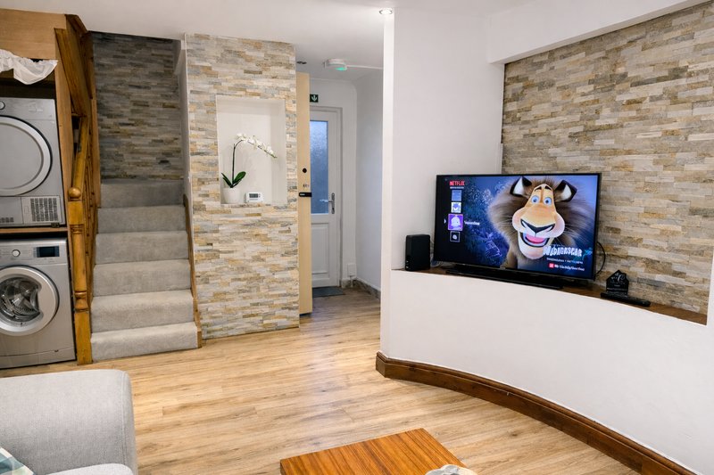 Open-plan living space with wooden flooring, brick accent wall, TV, and integrated laundry appliances