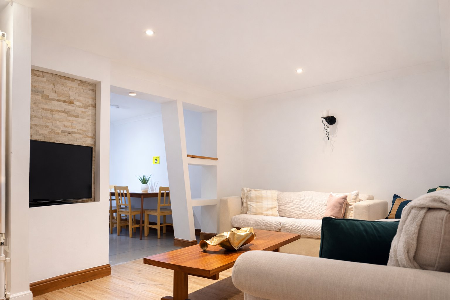 Open-plan living room with cream sofas, wooden coffee table, and modern kitchen visible