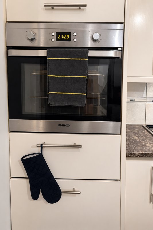 Built-in kitchen oven with stainless steel trim and black oven gloves hanging below