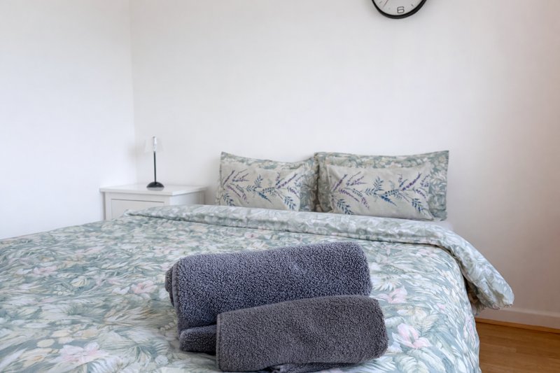 Bedroom with double bed, patterned bedding, rolled towels, and wall clock