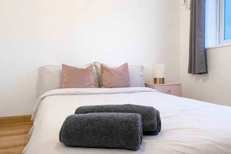 Bright bedroom with double bed, decorative pillows, rolled towels, and wooden flooring