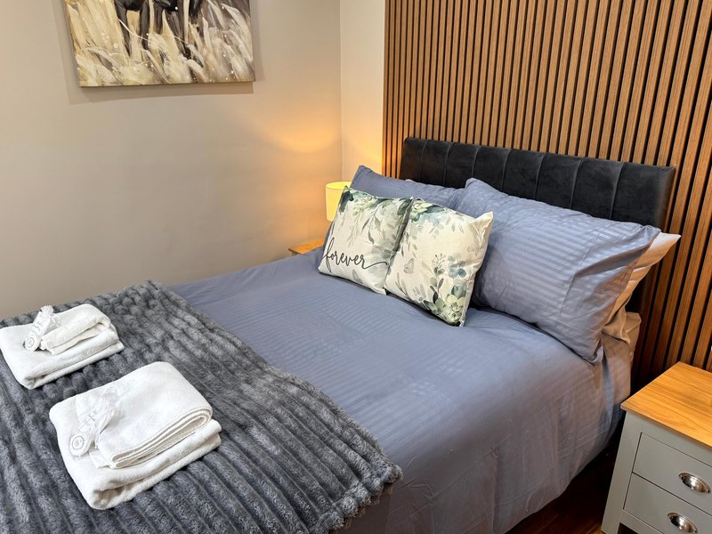 Modern bedroom with blue-grey bed, black headboard, decorative pillows and folded towels