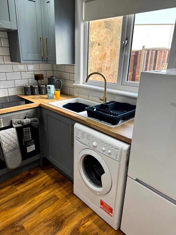 Modern kitchen with washing machine, sink, wooden countertop and window overlooking cityscape