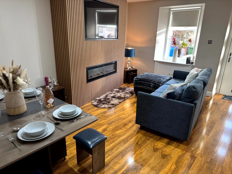 Open-plan living area with dining table, dark sofa, fireplace and wooden flooring