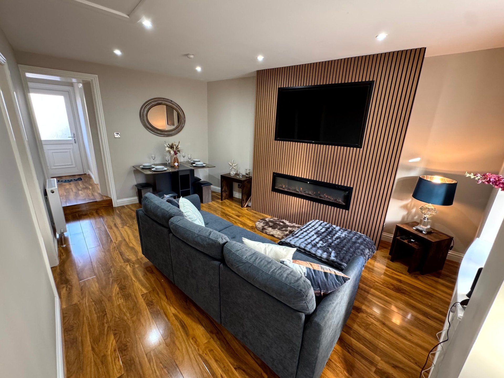 Modern living room with gray sofa, wall-mounted TV, wooden flooring and fireplace feature
