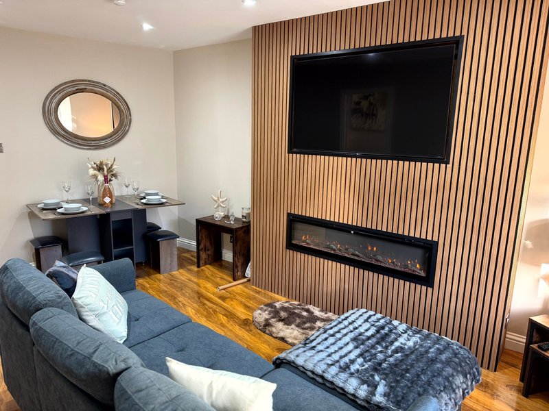 Modern living room with blue sofa, wall-mounted TV, fireplace, and wooden flooring