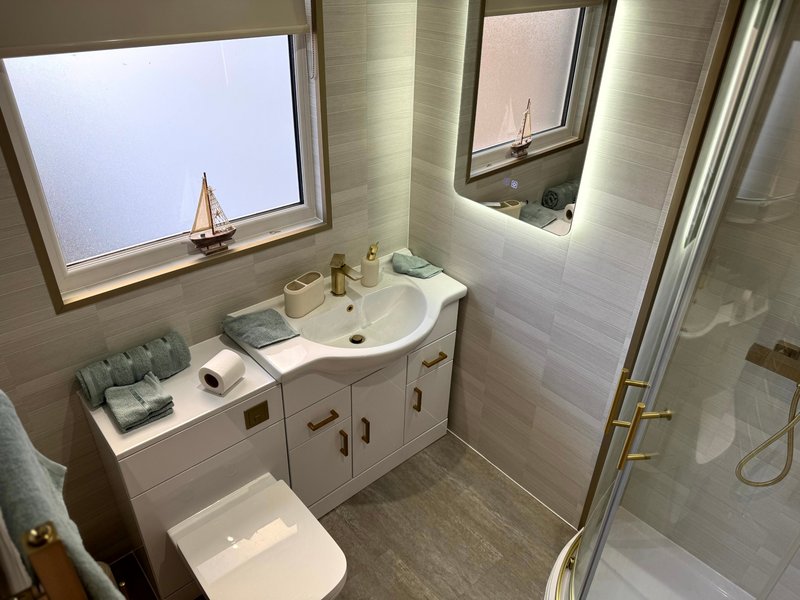 Bright bathroom with white vanity, circular sink, mirror, window, toilet and shower enclosure