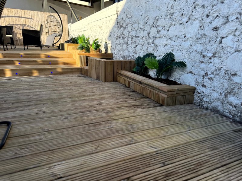 Wooden deck terrace with planter boxes, white brick wall, and interior spaces visible