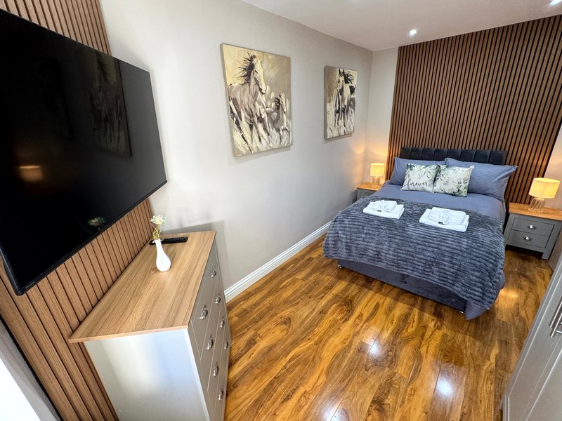 Modern bedroom with blue bed, wooden floor, wall-mounted TV, and framed artwork