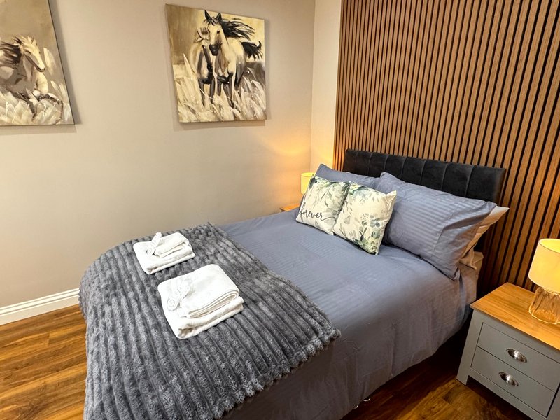 Bedroom with double bed, grey bedding, decorative pillows, wall art, wooden flooring and bedside lamp