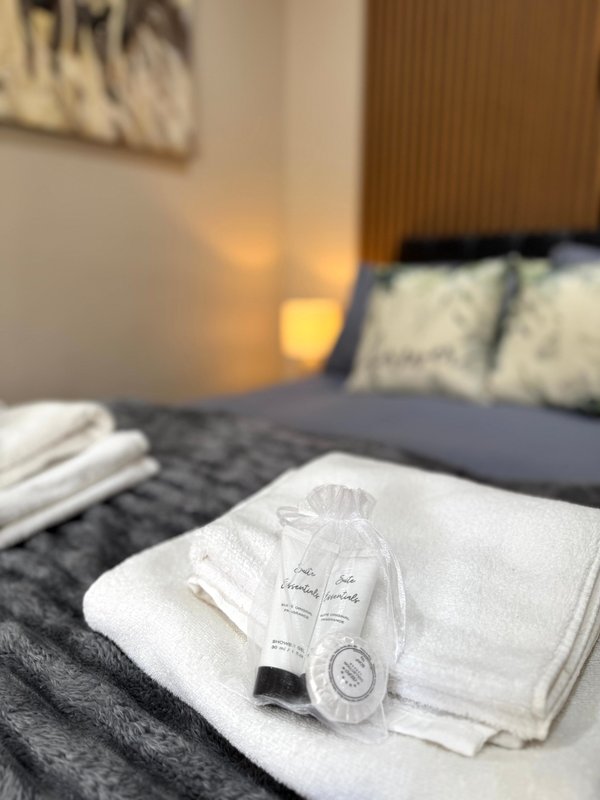 Bedroom with white towels, toiletries, and dark bedding on bed with pillows