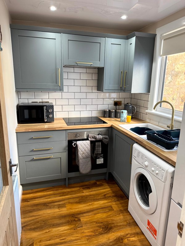 Modern kitchen with grey cabinetry, wooden worktops, white subway tile splashback, integrated appliances and washing machine