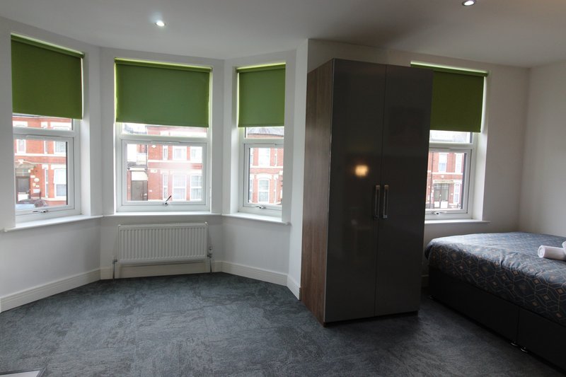Modern bedroom with bay windows, green blinds, dark wardrobe and single bed