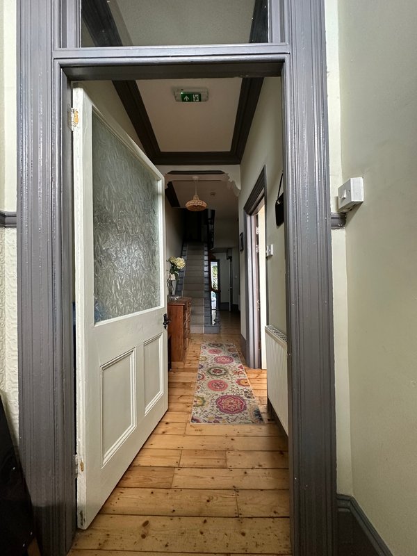 Long narrow hallway with wooden floorboards, patterned runner rug, white panelled doors and grey walls