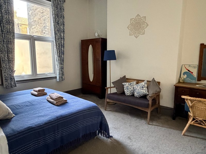 Bedroom with double bed, wooden furniture, window with curtains, and seating area