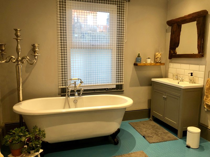 Bathroom with freestanding white bathtub, vanity sink, mirror, window with checkered curtains
