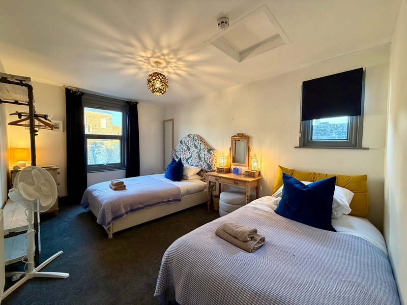 Bright twin bedroom with two beds, blue and gold cushions, pendant light and windows