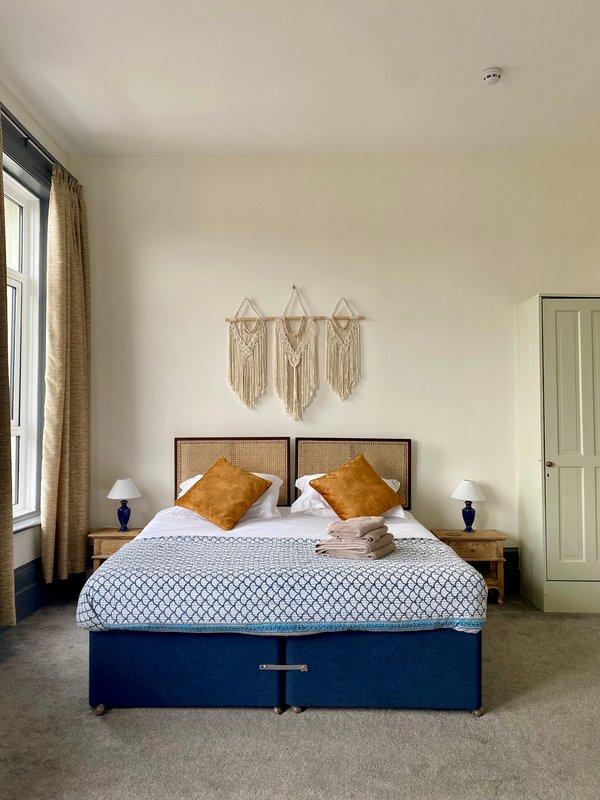 Bedroom with double bed, gold cushions, macramé wall hangings, bedside lamps and curtains