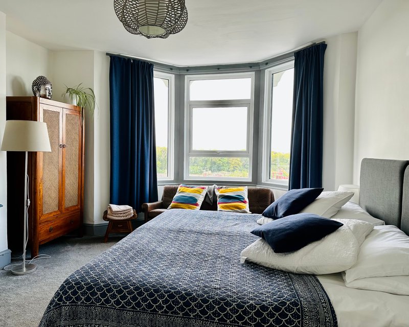 Modern bedroom with double bed, bay window with blue curtains, wooden wardrobe and pendant lamp