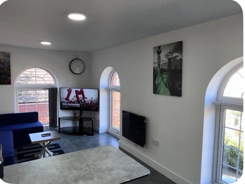 Modern living room with blue sofa, TV, clock, and large arched windows overlooking cityscape