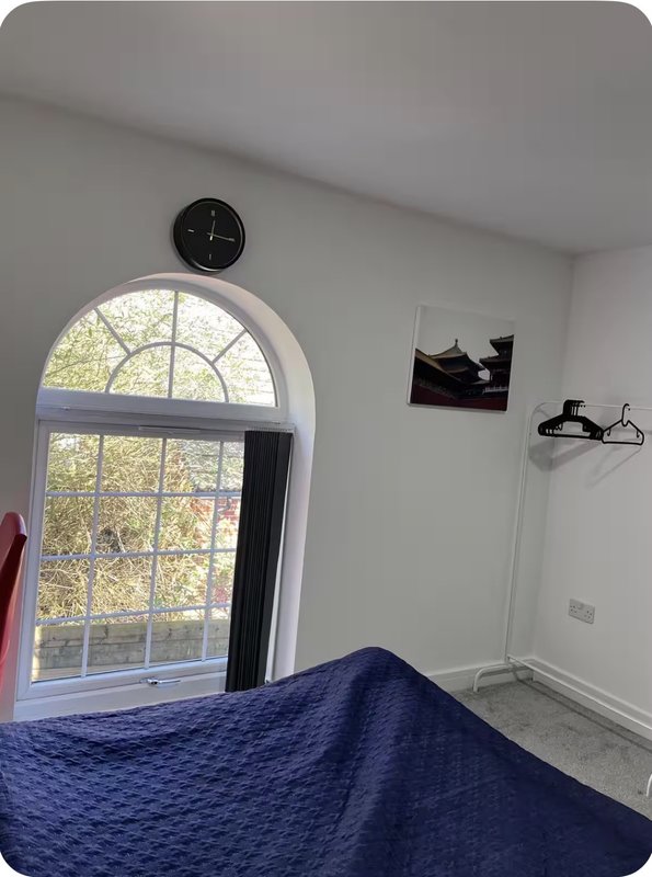 Bright bedroom with arched window, blue bedding, wall clock, and minimal decor
