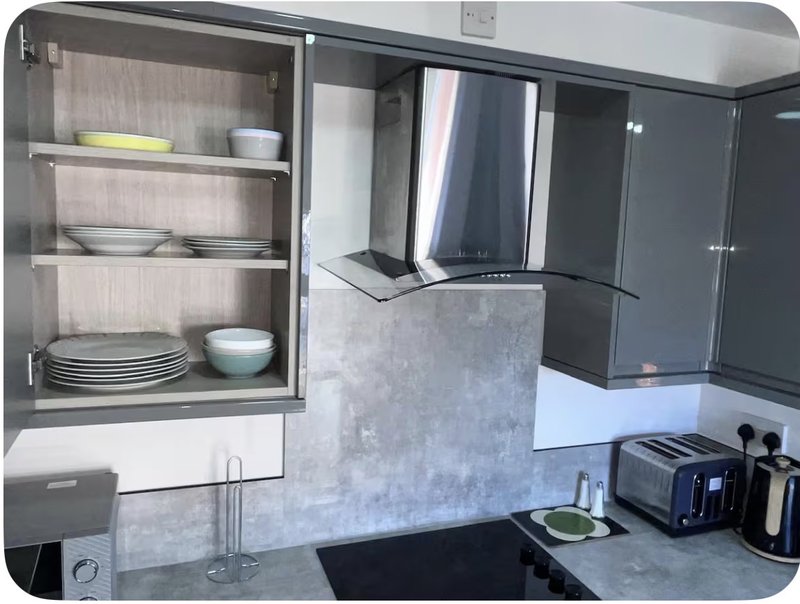 Modern kitchen with dark cabinetry, concrete backsplash, open shelving with dishes, and black countertop