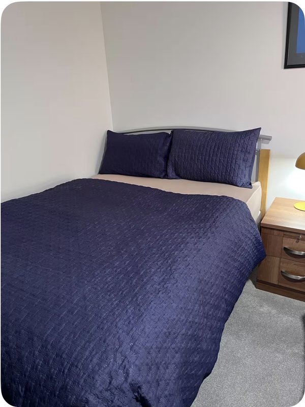 Bedroom with double bed, navy bedding, wooden bedside table and white walls