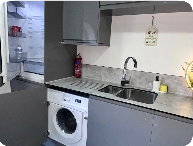 Modern kitchen with grey cabinetry, stainless steel sink, white washing machine and window view