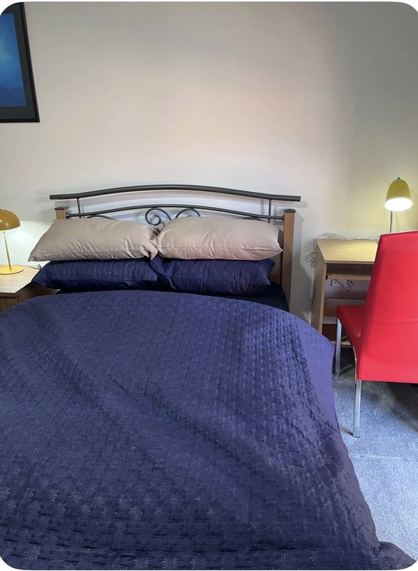 Bedroom with double bed, metal headboard, navy bedding, pillows, bedside lamps and red chair