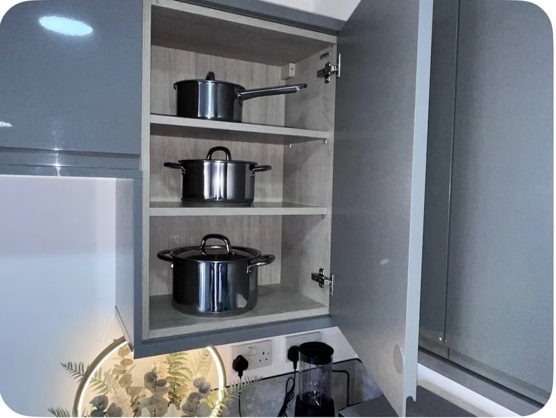 Open kitchen cabinet with stainless steel cookware and pots on shelves