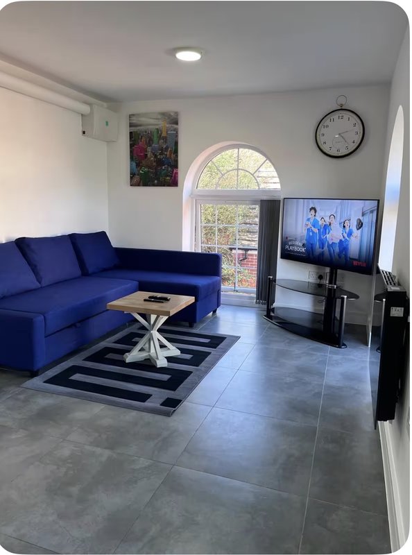 Modern living room with blue sofa, TV, arched window door and neutral tiling