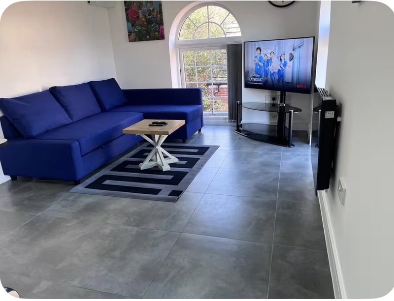Modern living room with blue sectional sofa, gray tile flooring, and wall-mounted TV