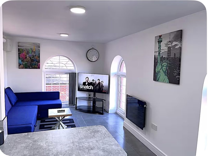 Modern living room with blue sofa, TV stand, wall art, and arched windows with natural light