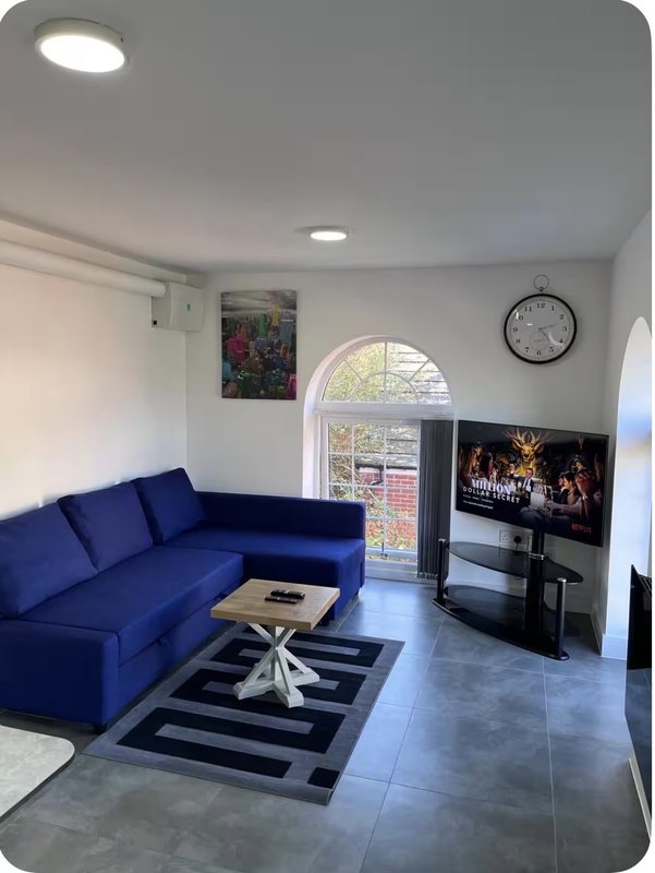 Modern living room with blue corner sofa, TV, arched window and wall clock