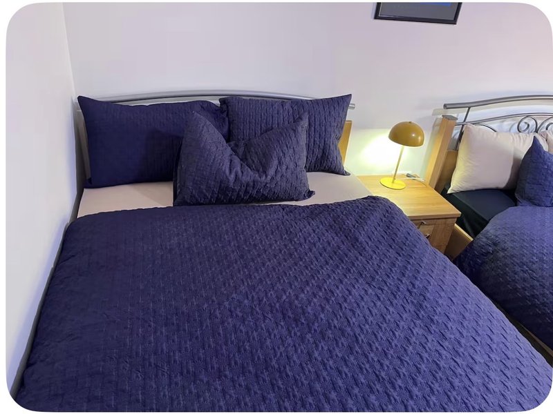 Bedroom with double bed, navy bedding, decorative pillows, wooden bedside table and lamp