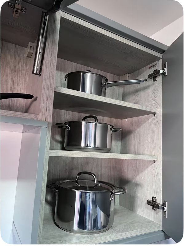 Open kitchen cabinet with stainless steel pots and pans on white shelves
