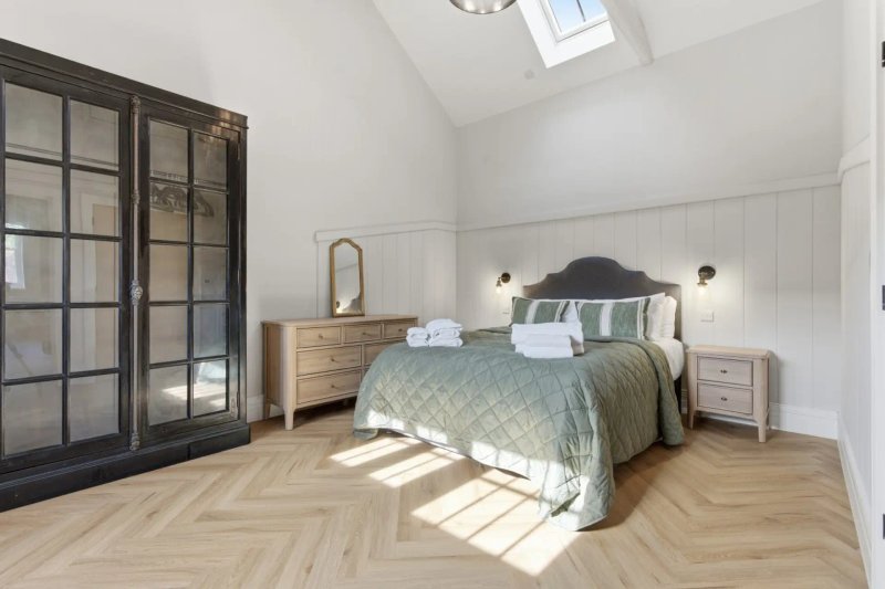 Bright attic bedroom with double bed, wooden flooring, black wardrobe and white walls