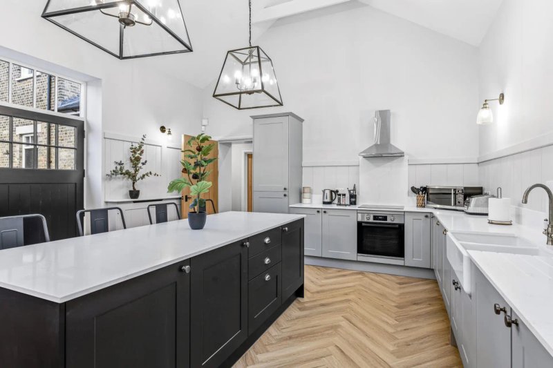 Modern kitchen with black island, white cabinetry, herringbone wood flooring and pendant lighting
