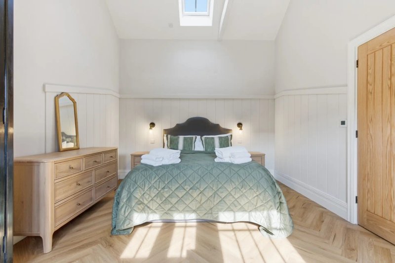 Bright modern bedroom with quilted bed, wooden dresser, skylight and wooden flooring