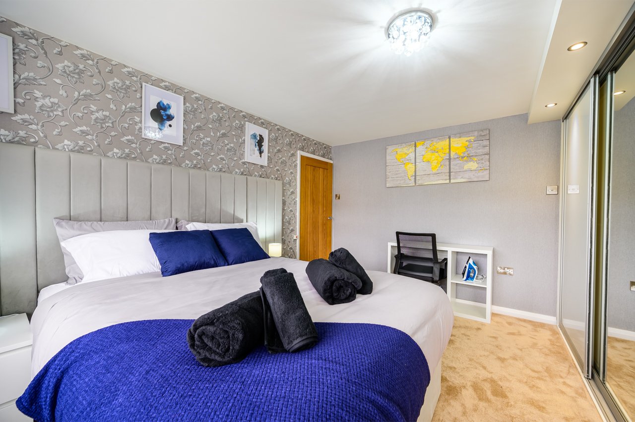 Modern bedroom with blue and white bedding, padded headboard, wooden flooring and wall art