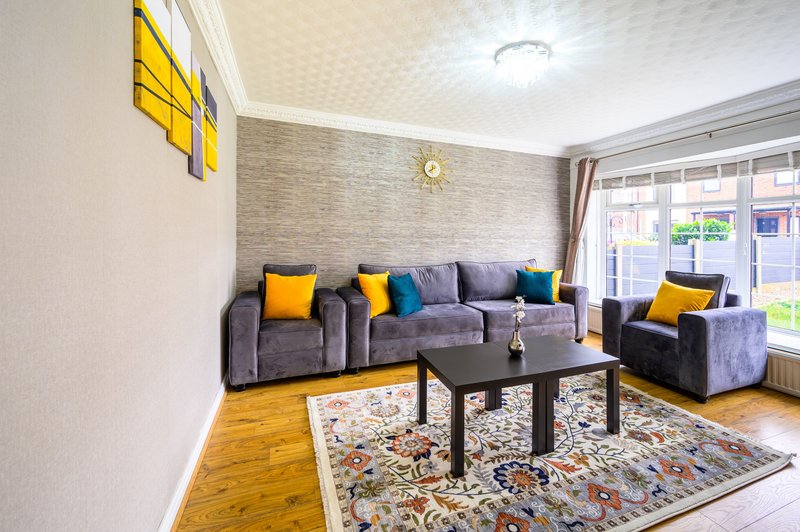 Modern living room with gray upholstered seating, colorful cushions, black coffee table, and large windows with street view