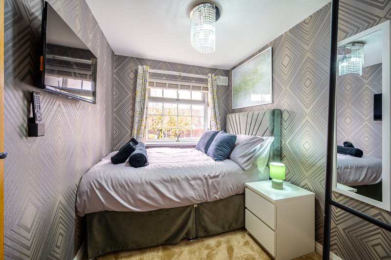 Bright bedroom with double bed, geometric wallpaper, window with natural light, and mirrored wardrobe