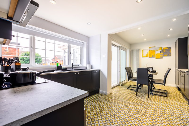 Modern open-plan kitchen and dining area with black cabinetry, marble countertop and yellow patterned flooring